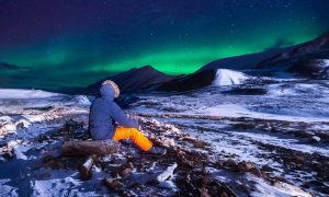 a man sits on some rocks looking at the northern lights